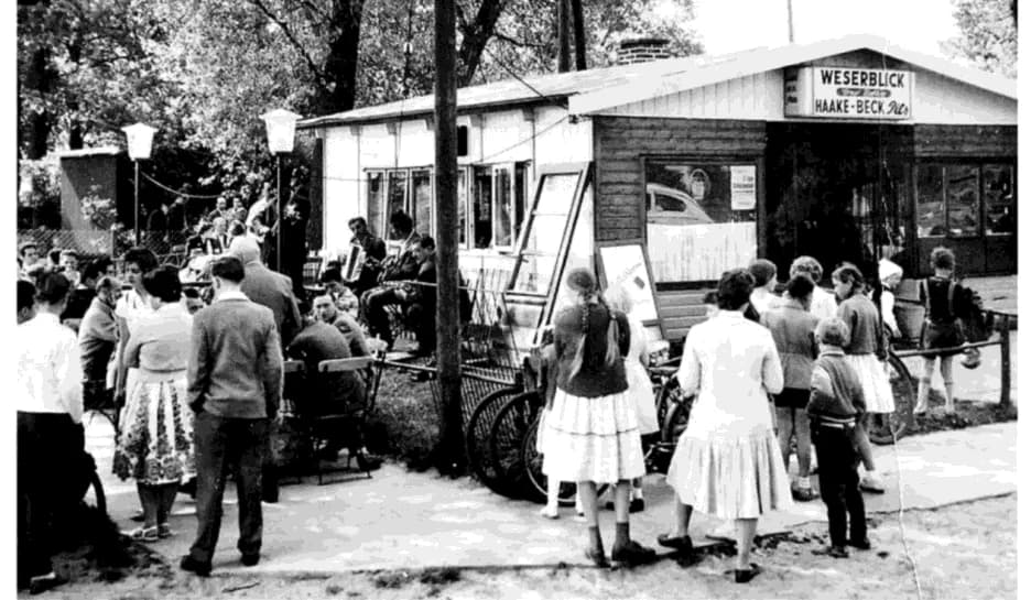 Schwarzweißfoto von 1958: Ausflügler in Sommerkleidung vor der Holzbaracke mit dem Schild Weserblick