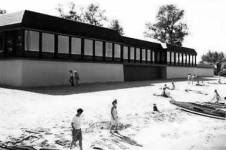 Schwarzweißfoto: das Restaurant von 1979 mit langem Fensterband auf hohem Sockel, davor Kinder am Strand